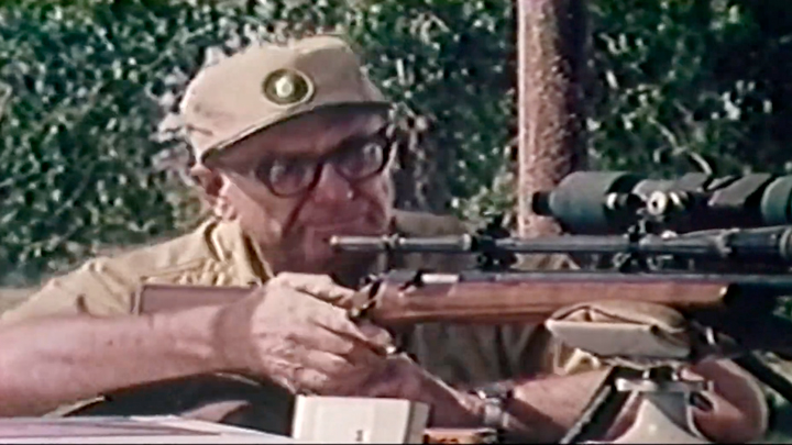 Vintage image of man shooting wood-stocked rifle with scope at a shooting bench.