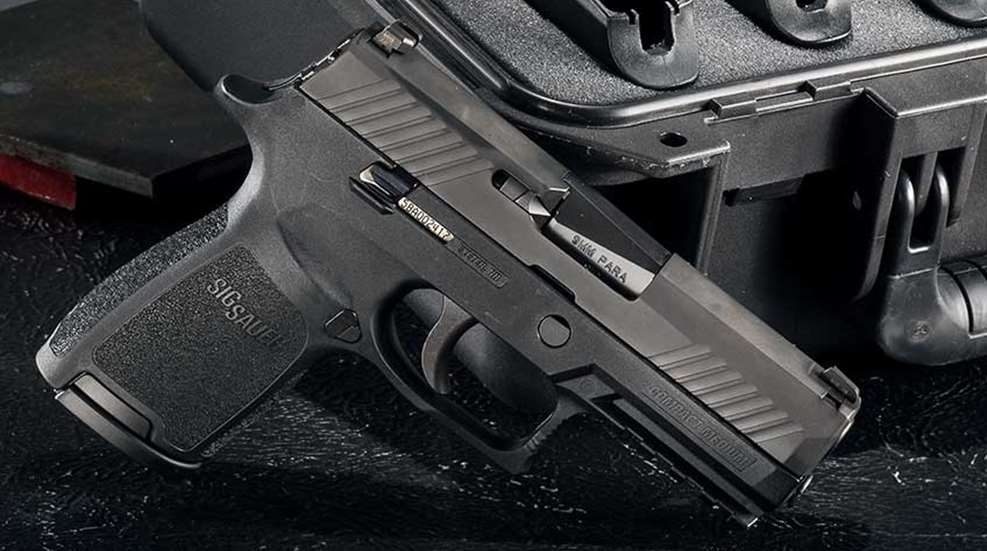 A black SIG Sauer P320 propped against a black, hard-sided gun case.
