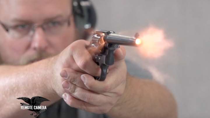 Man wearing protective gear while shooting a revolver with fire blast coming from the muzzle.