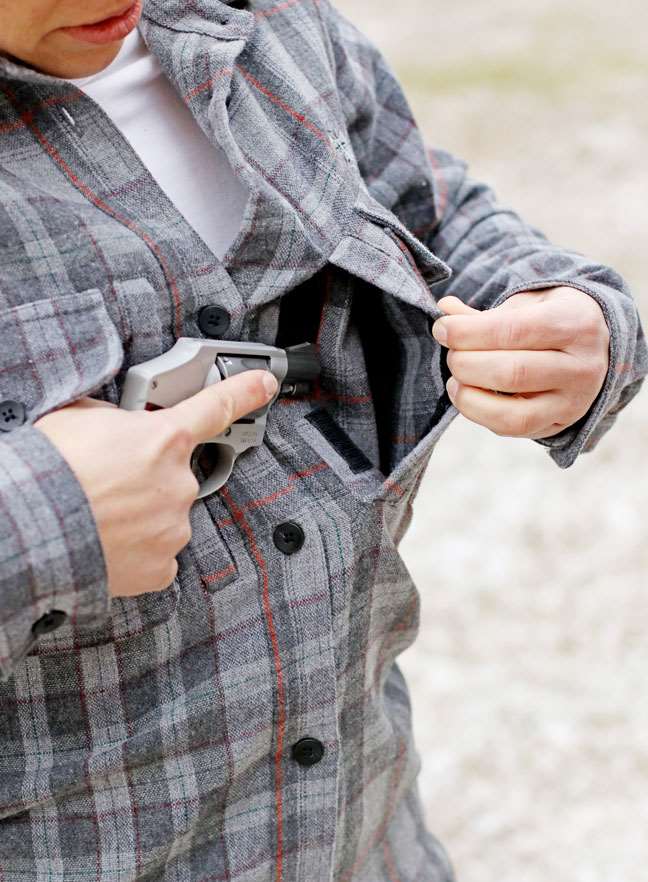 Woman in black and gray checkered shirt drawing pistol from shirt pocket.