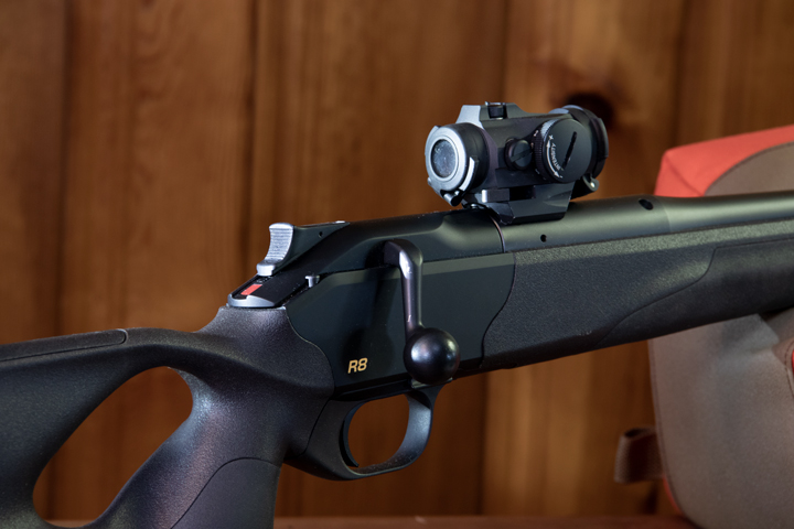 Close-up view of a rifle and optic with wooden background.