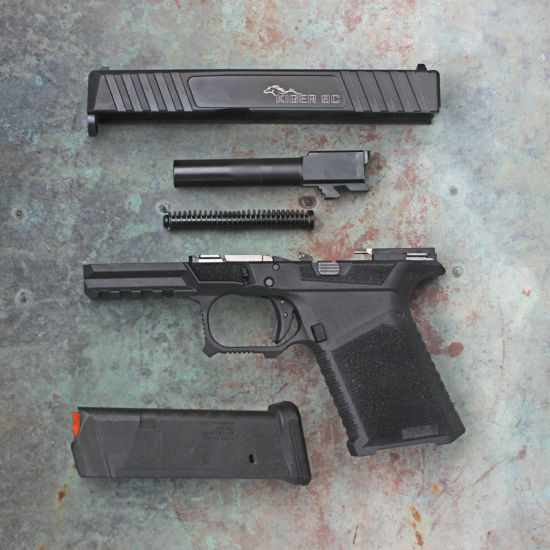 Kiger 9c 9mm pistol disassembled view arrangement of gun parts handgun metal plastic barrel spring slide magazine frame weathered-steel background