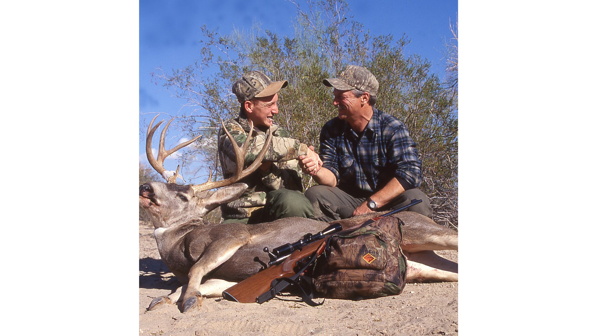 men shaking hands congratulatory hunters harvest mule deer rifle outdoors