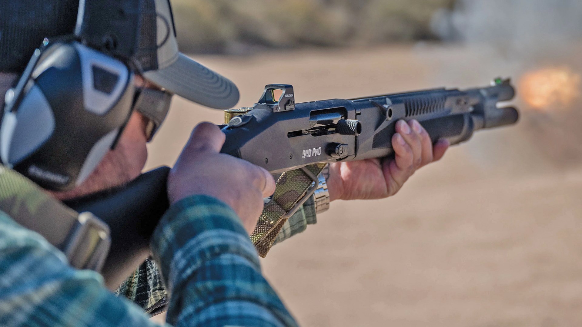Man firing a Mossberg 940 Pro Tactical shotgun on an outoor range.
