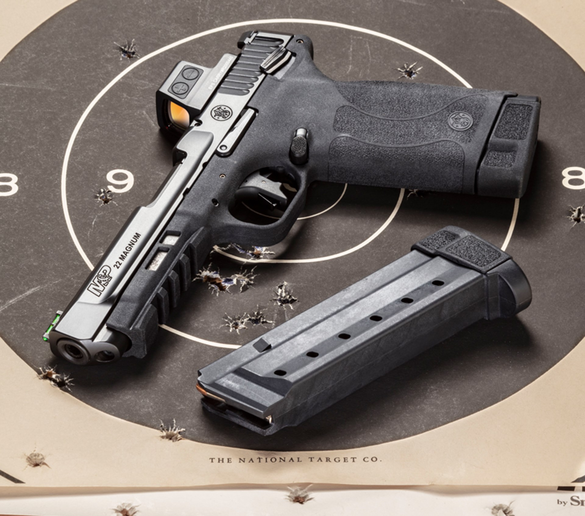 The Smith & Wesson M&P 22 Magnum laying on a shot bullseye target with an empty black magazine next to it.
