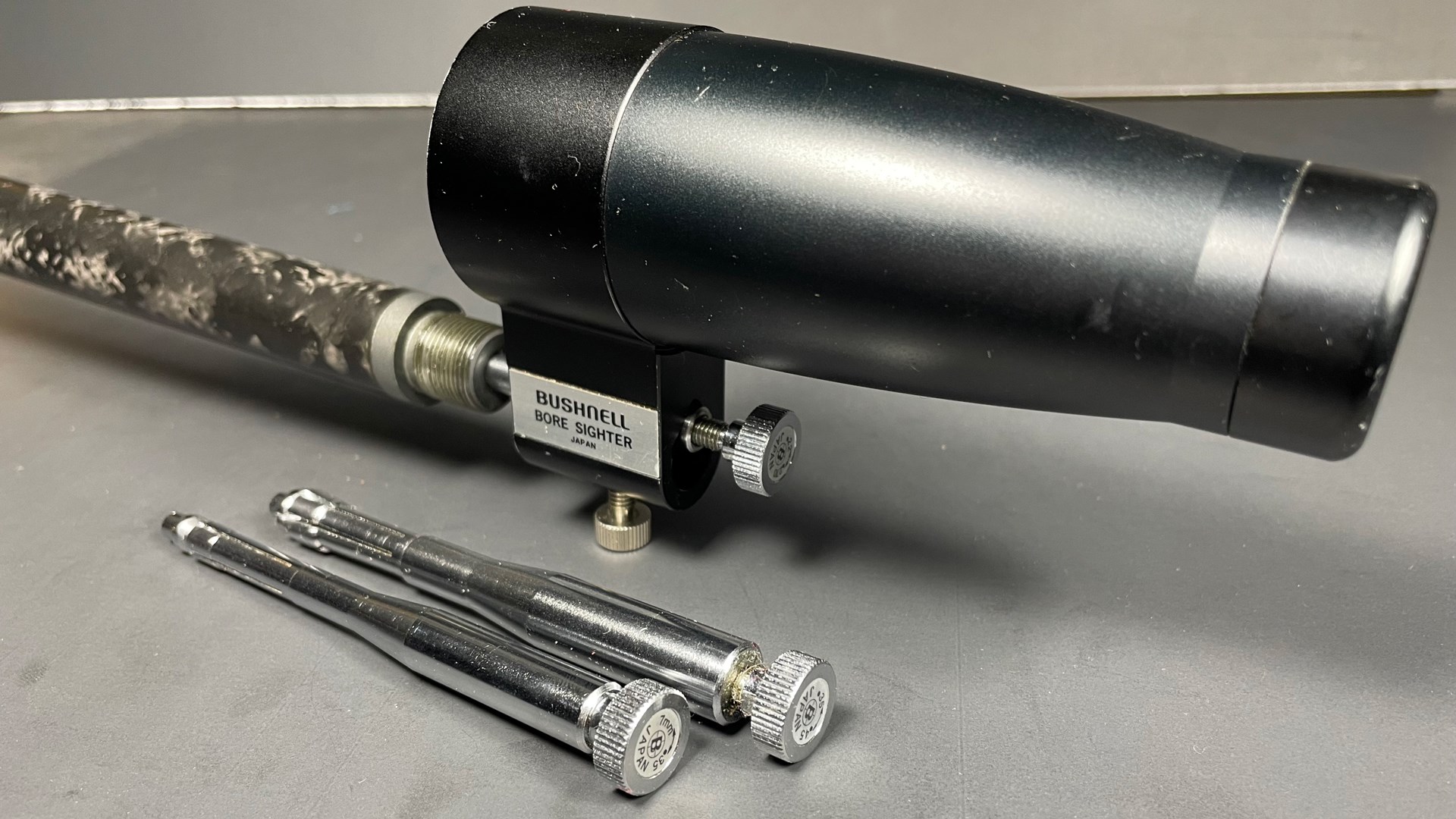 black round cylinder attached to carbon-fiber barrel tool Bushnell bore sighter