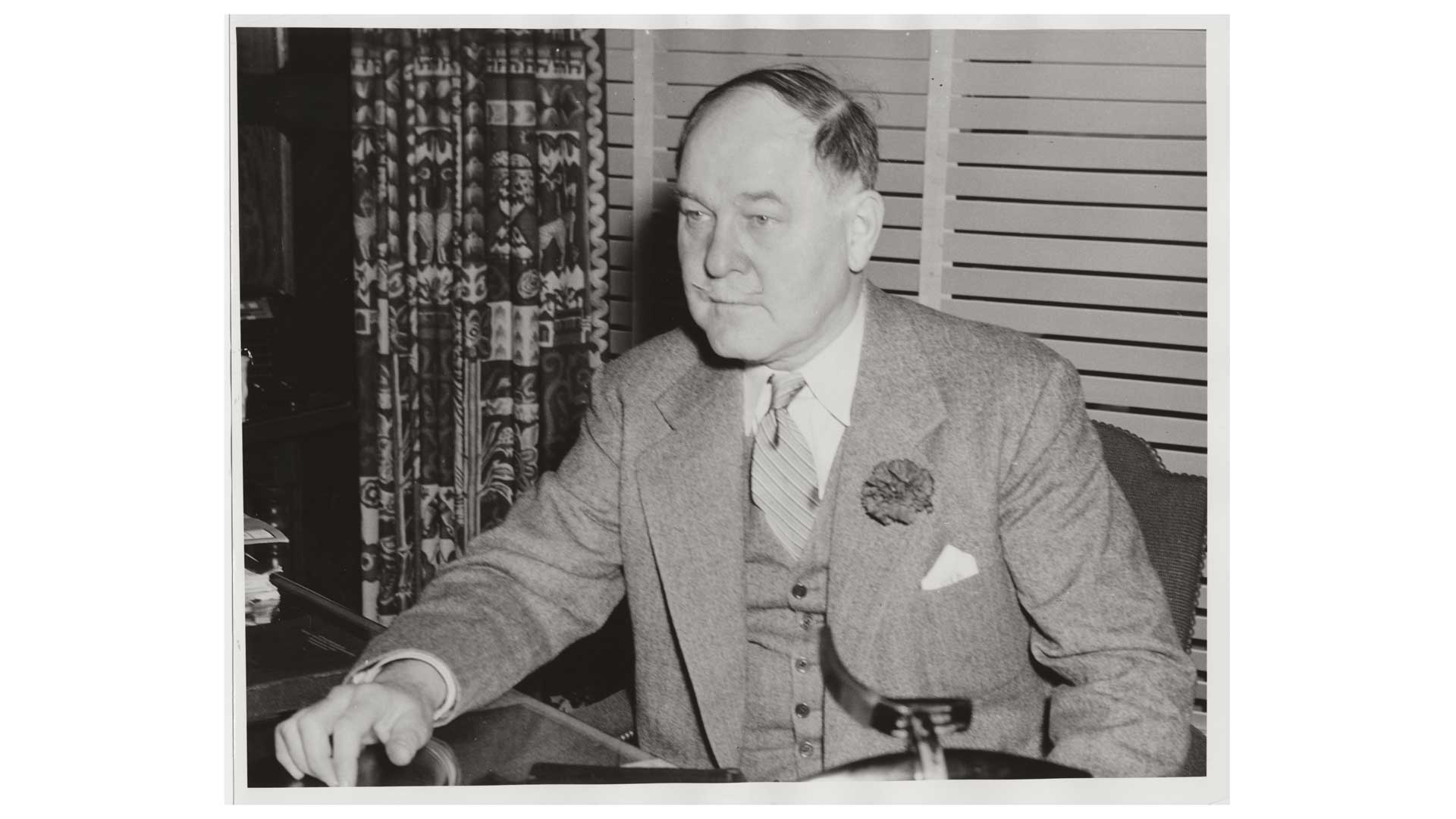 black and white image of man in suit sitting at table office