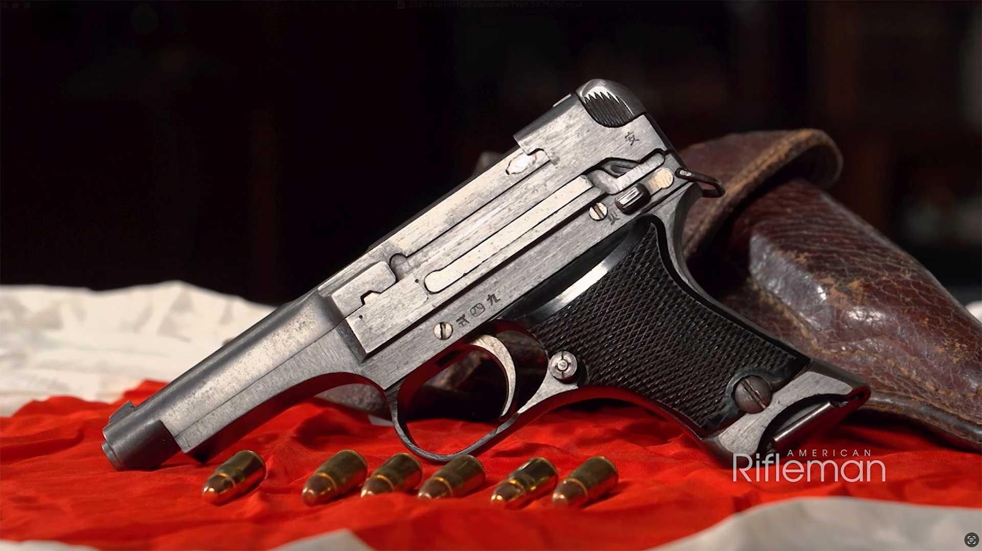 Left side of the Japanese Type 94 handgun, resting atop a Japanese flag with a leather holster in the background.
