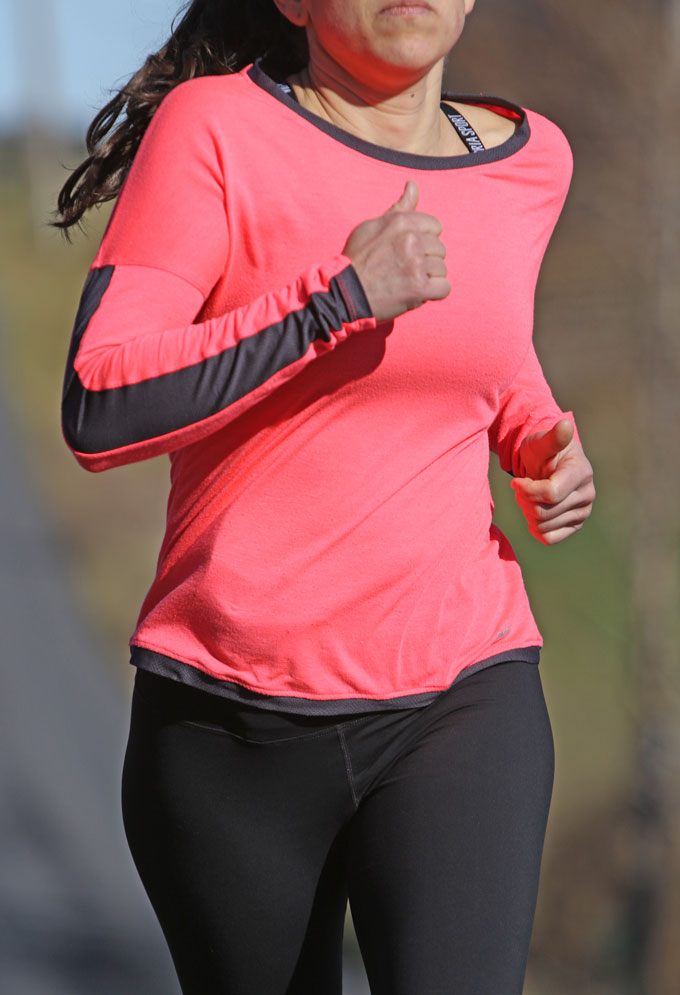 Woman jogging outdoors in pink and black outfit designed for concealed carry of a pistol.