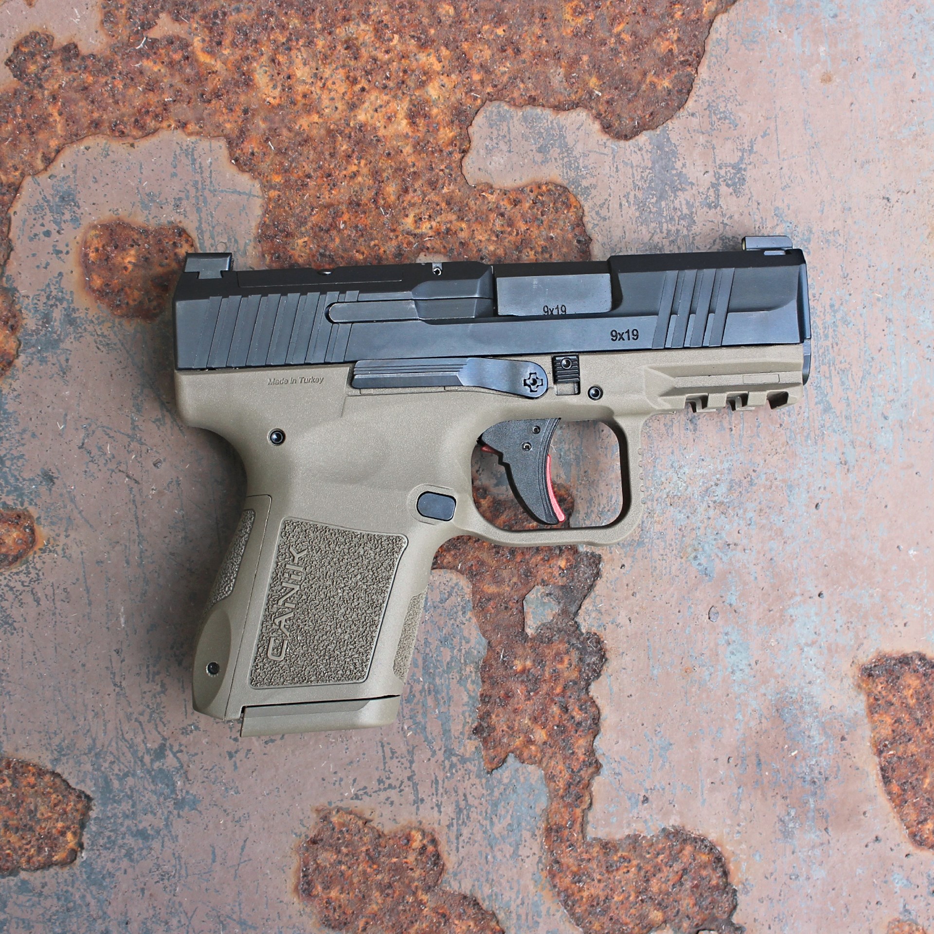 Canik MC9 right-side view on rusty steel plate 9 mm pistol handgun semi-automatic gun two-tone black FDE