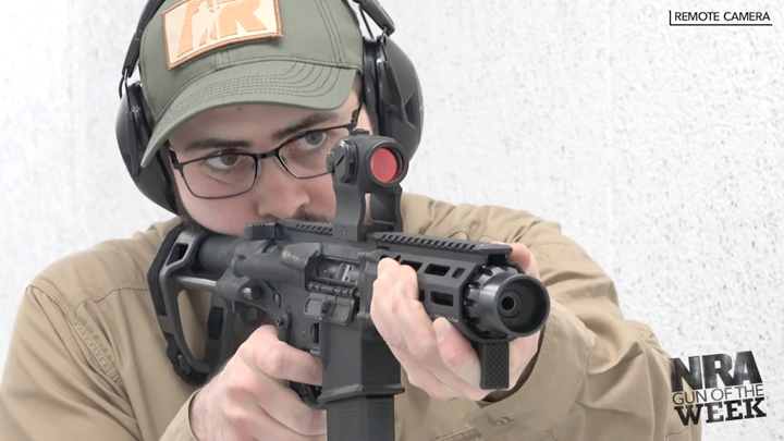 Man wearing a ballcap and protective shooting gear shooting an AR-15 pistol on a shooting range.