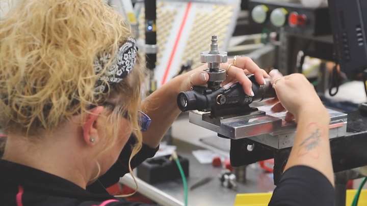 Woman in a factory assembling a Trijicon optic.