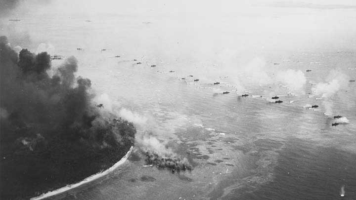 The first wave of LVTs moves toward the invasion beaches of Peleliu , on Sept. 15, 1944, passing through the inshore bombardment line of LCI gunboats. Cruisers and battleships are bombarding from the distance. The landing area is almost totally hidden in dust and smoke. Photographed by a floatplane from USS HONOLULU (CL-48). U.S. Navy photograph # 80-G-283533.