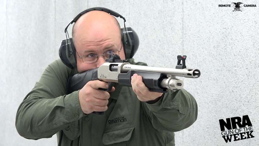 Man wearing green shirt ear muffs shooting silver shotgun