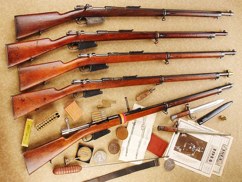 5 Belgian Model 1889 Mausers on a cream background surrounded by period letters, posters, medals, cartridge boxes and a bayonet.