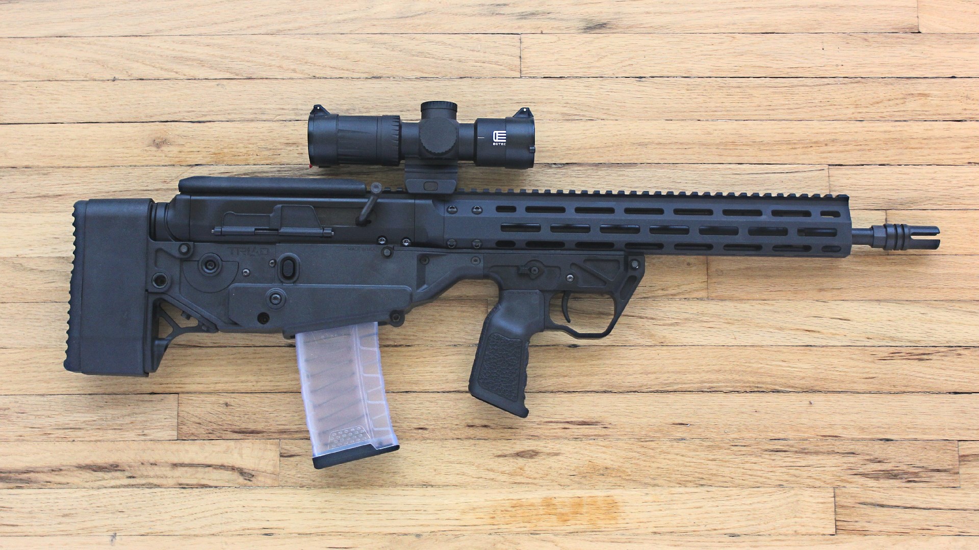 A3 Triad Bullpup rights-side view fully assembled carbine shown with clear magazine and eotech optic attached wood flooring background