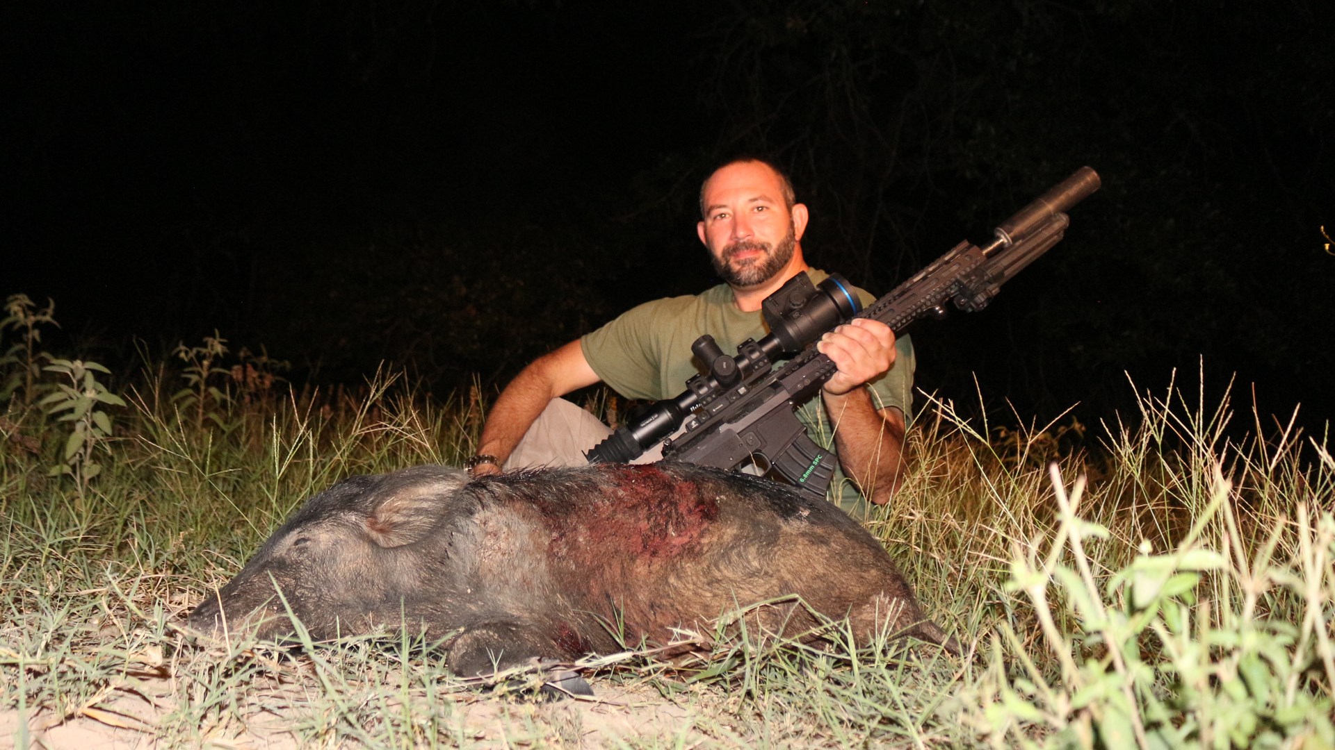 Author Frank Melloni in darkness with harvest wild pig boar shown holding ar-15 rifle with Pulsar thermal imaging and suppressor