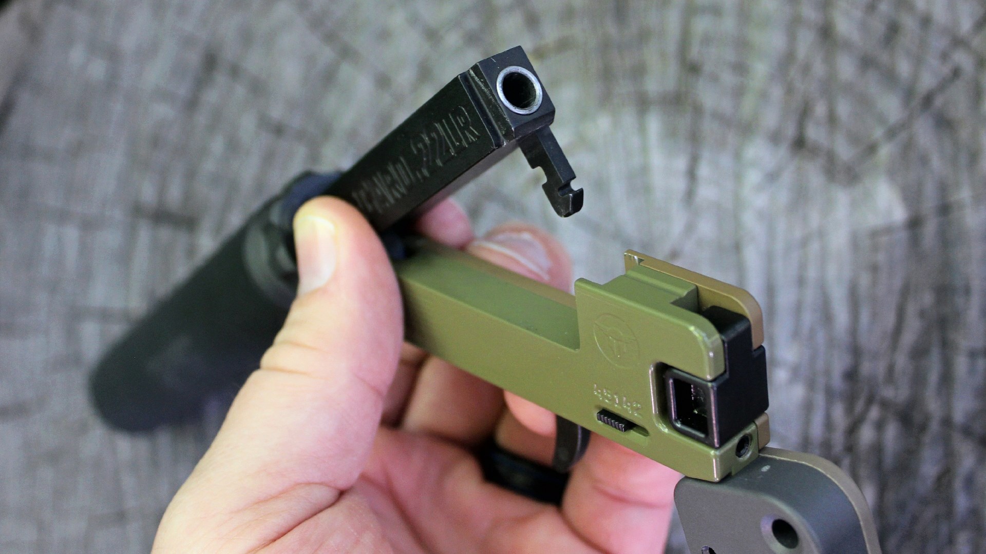 Trailblazer Firearms LifeCard single-shot pistol in hand detailing barrel latch mechanism under barrel wood background soft focus