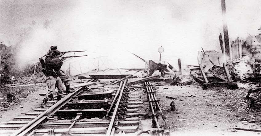 2 Belgian rifleman armed with Model 1889 Mausers stand on a railroad trestle, firing across the wreckage of a village at advancing German forces.