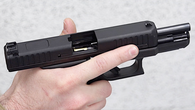 Glock G44 rimfire pistol in shooter&#x27;s hand with slide locked back with view of loaded magazine inside the gun.