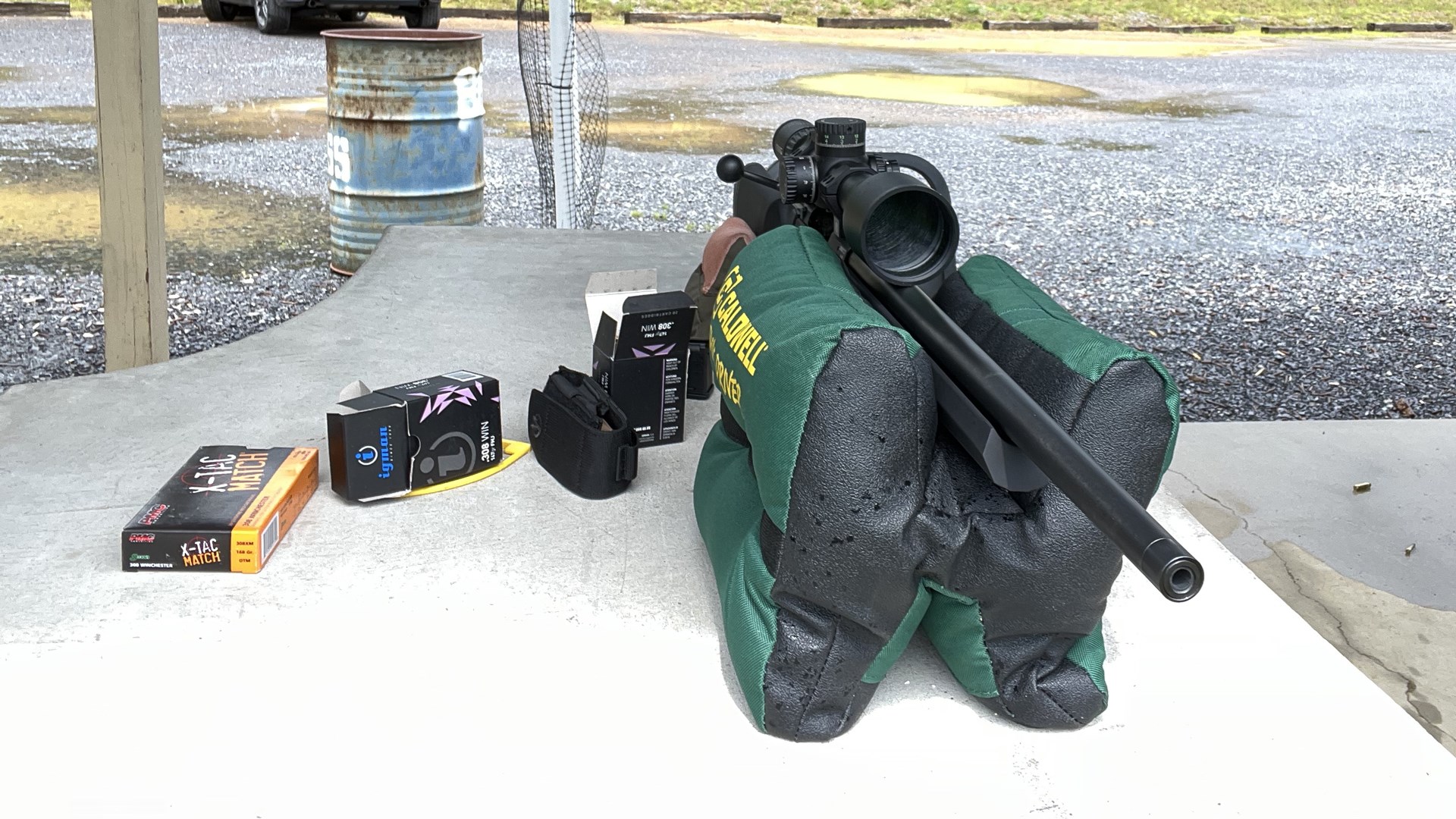 CZ 600 Alpha bolt-action rifle in caldwell range back shown on concrete bench under outdoor range pavilion and ammunition gravel parking lot background with steel metal drum off to side tires car