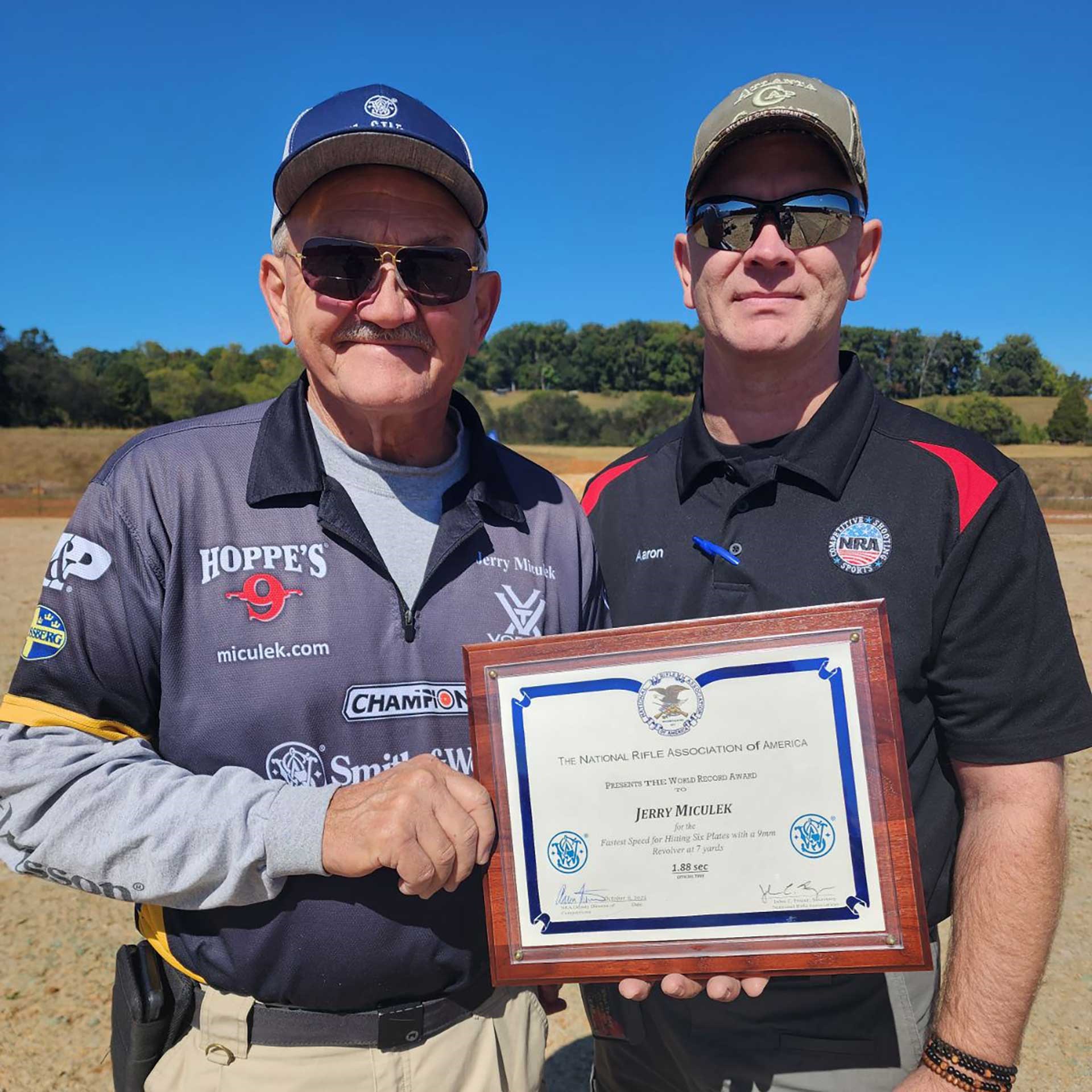 Jerry Miculek and Aaron Farmer stand with Jerry's NRA World Record plaque.