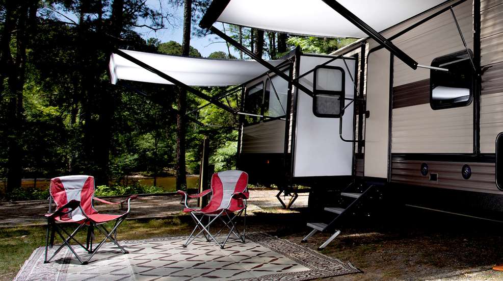 RV camper parked with chairs awning outdoors river background camping campsite