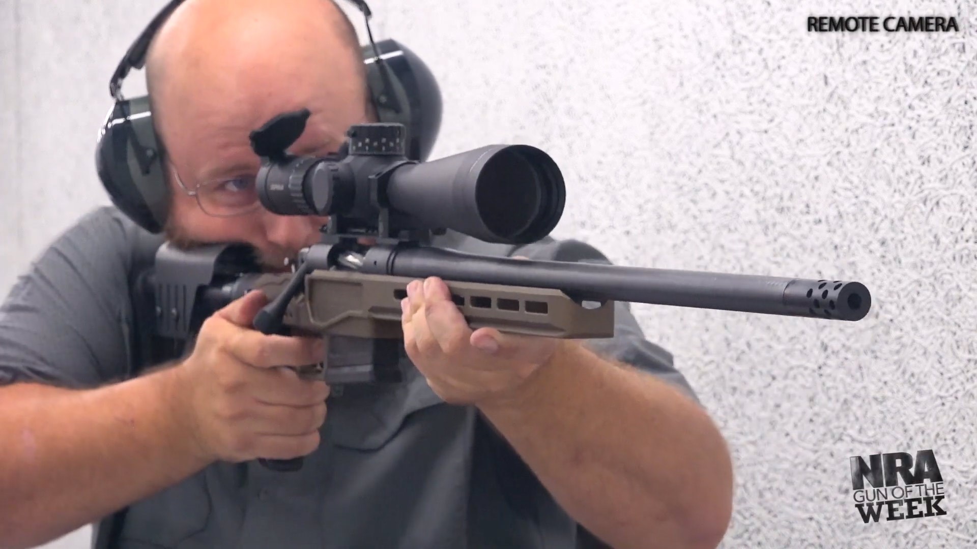 Man firing bolt-action bergara mglite rifle carbon fiber barrel white walls riflescope remote camera angle
