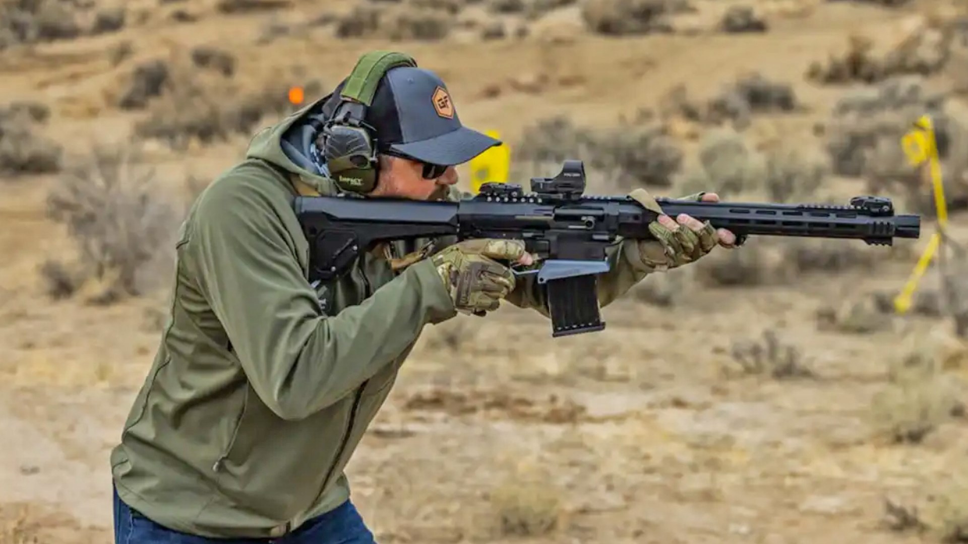 Man wearing a green jacket aiming the GForce Arms 12Hammer in a desert environment.