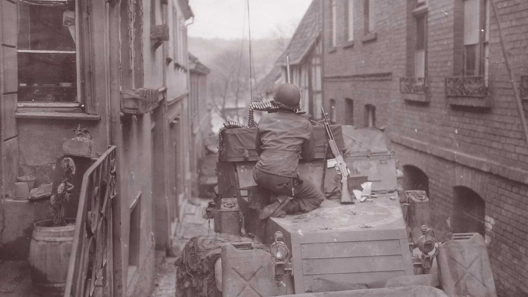 A crewman aboard an M3 halftrack engages snipers in Remagen town with Browning M2 .50 caliber machine gun.  Note the BAR to his left.