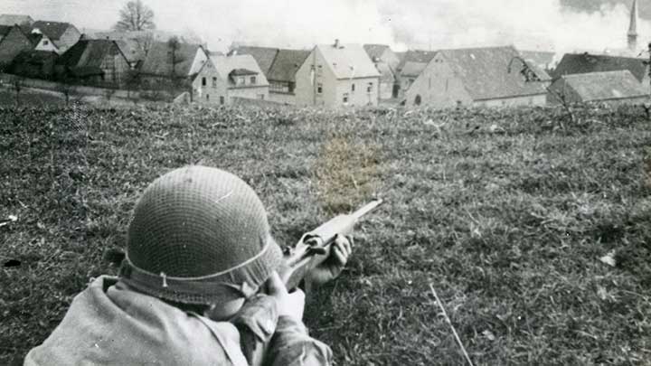 A G.I. with an M1 Carbine surveys the outskirts of Cologne while the city burns.