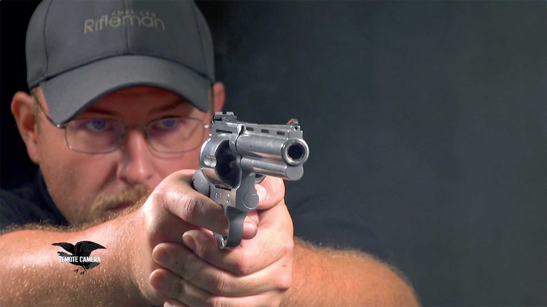 A man wearing a gray baseball hat aiming the Colt Anaconda revolver downrange.