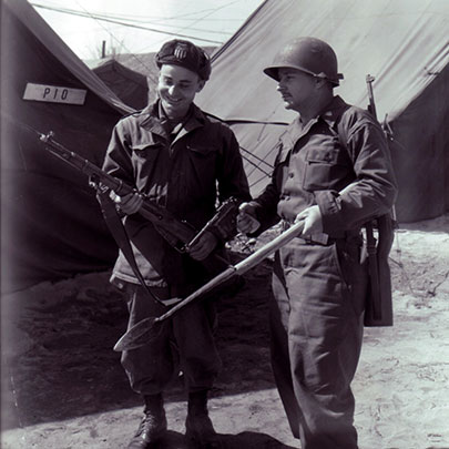 U.S. War Correspondents review captured communist weapons, ranging from a M1938 Carbine (modified to accept a bayonet), a Chinese Bolo Mauser (with a white grip) and a classic spear for the modern era.