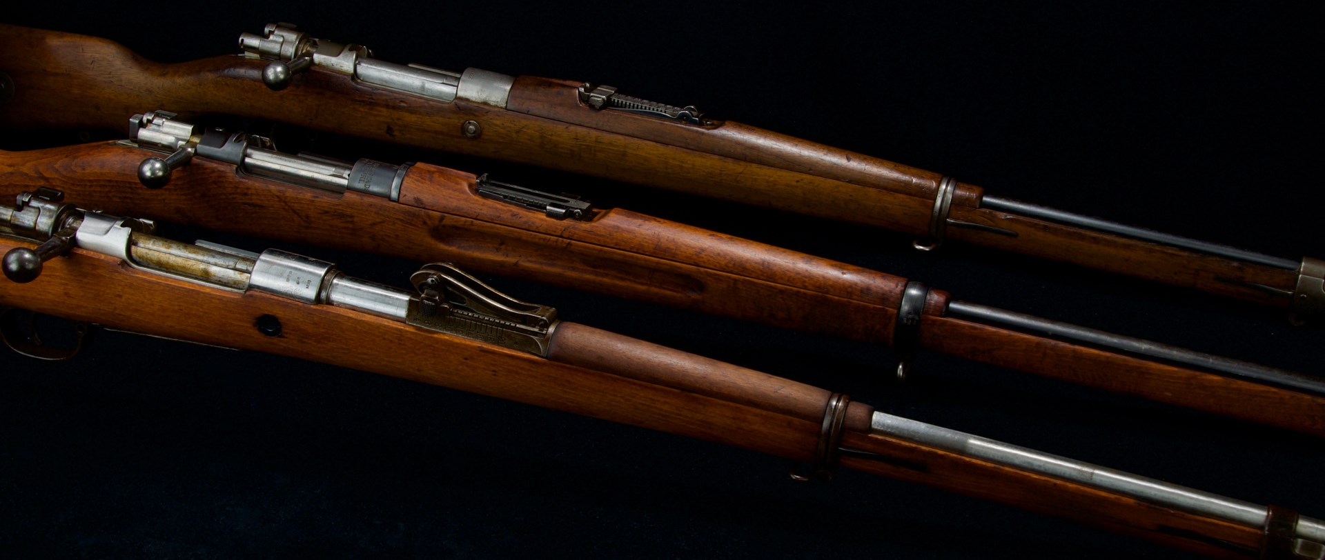 three mauser bolt-action rifles diagonal black background wood metal
