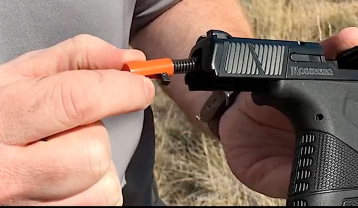 Mossberg pistol in hand with shooter removing orange-colored striker assembly from rear of the slide.