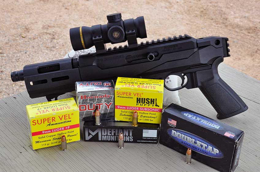 Ruger PC Charger pistol with leupold optic and five boxes of ammuntion positioned on shooting bench with sandbag
