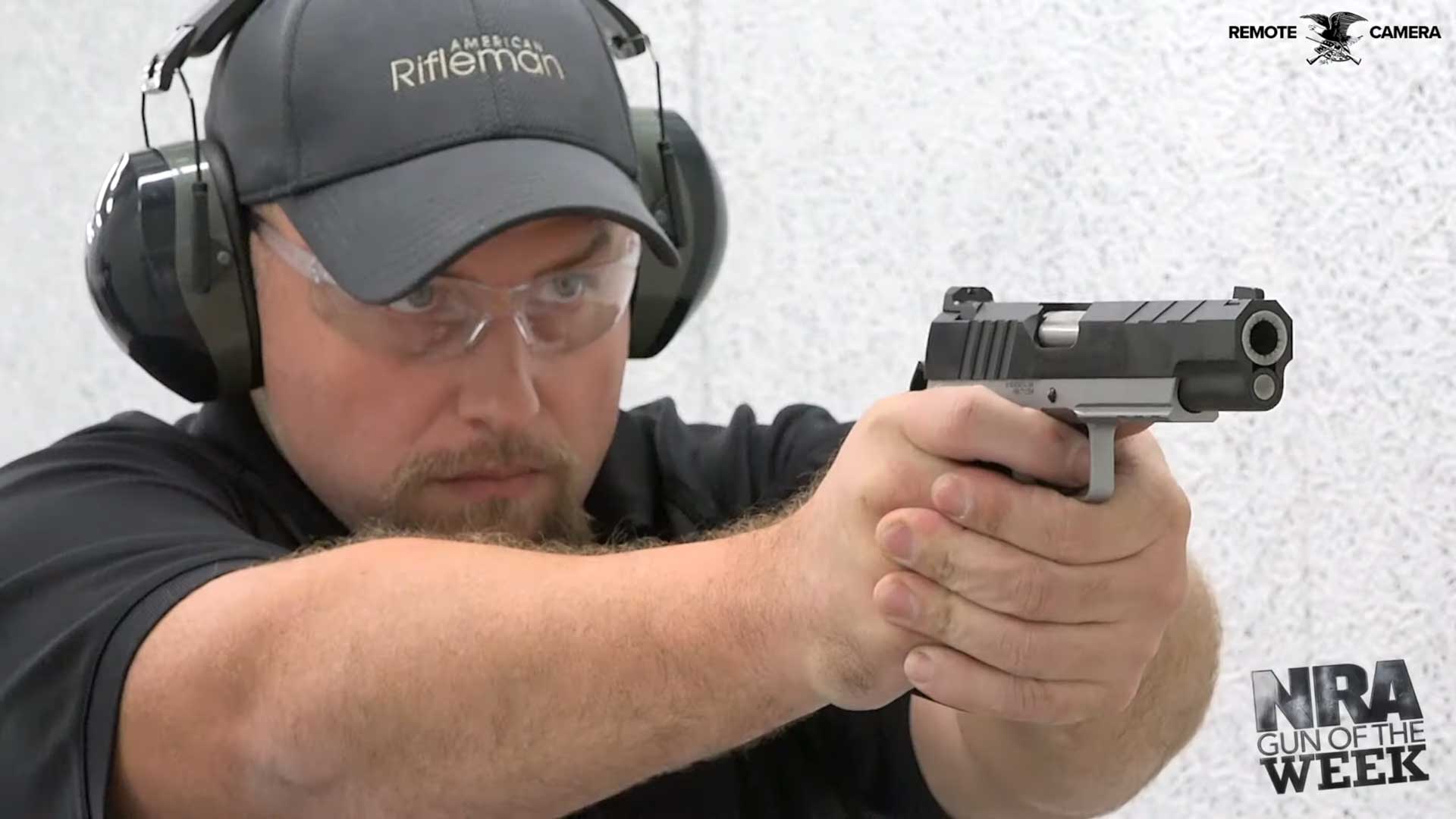 man wearing black shirt gray hat earmuffs glasses gun shooting target range pistol hangun