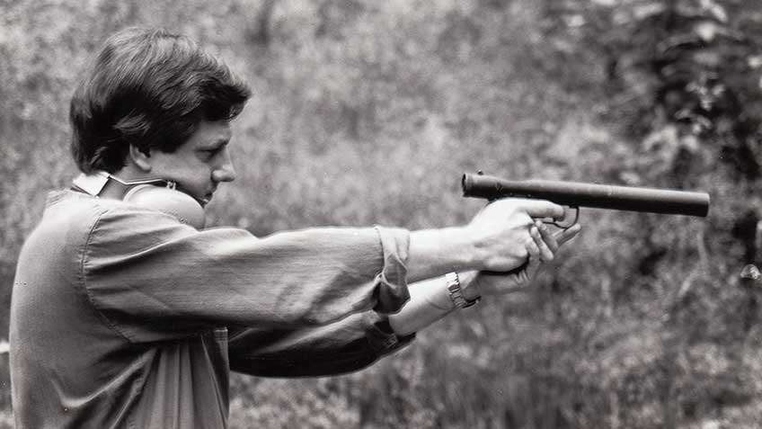 Man with hearing protection off ears and around neck shooting Welrod suppressed pistol demonstrating size and lack of need for hearing protection when using this suppressed pistol.