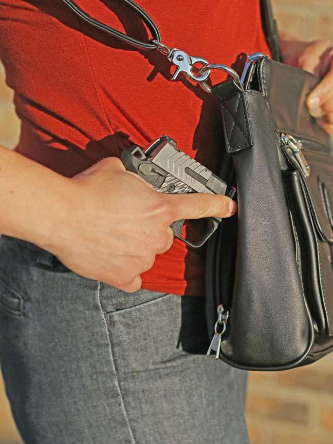 Right-side view of woman in red shirt and jeans withdrawing a pistol from a purse.