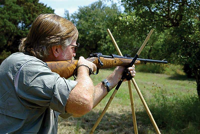 Man outdoors shooting rifle wooden sticks trees background