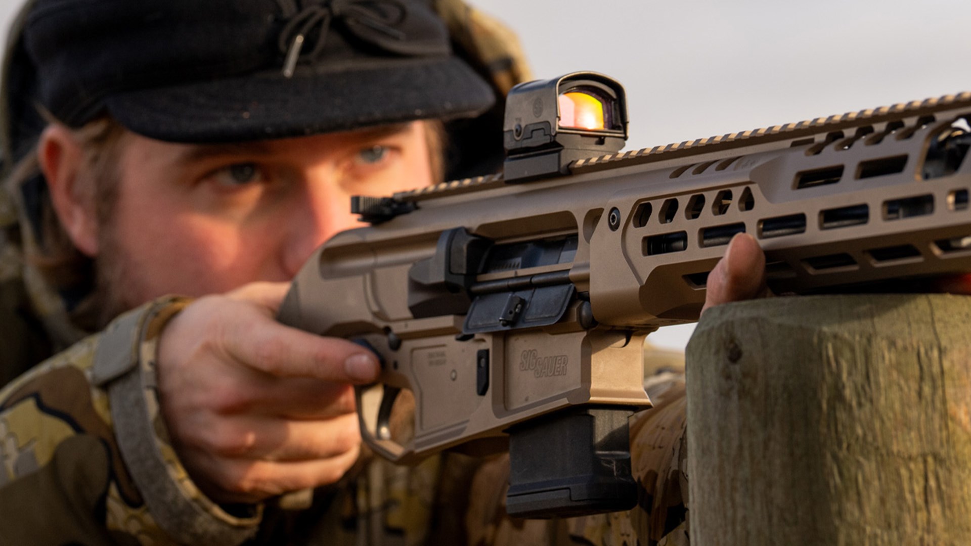 Man aiming SIG Sauer MCX Regulator while using a wooden fence post as a front rest.