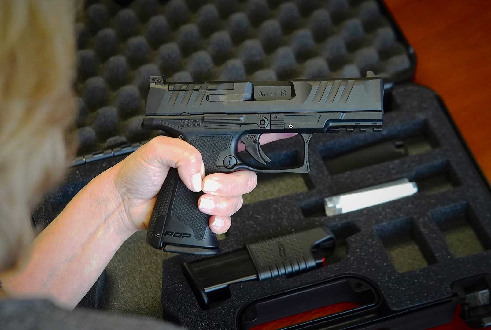 Woman holding the Walther Arms PDP F-Series handgun above a desk with an open handgun case underneath.