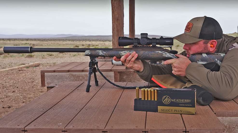A man aiming a Weatherby 307 series rifle over a wooden shooting bench.