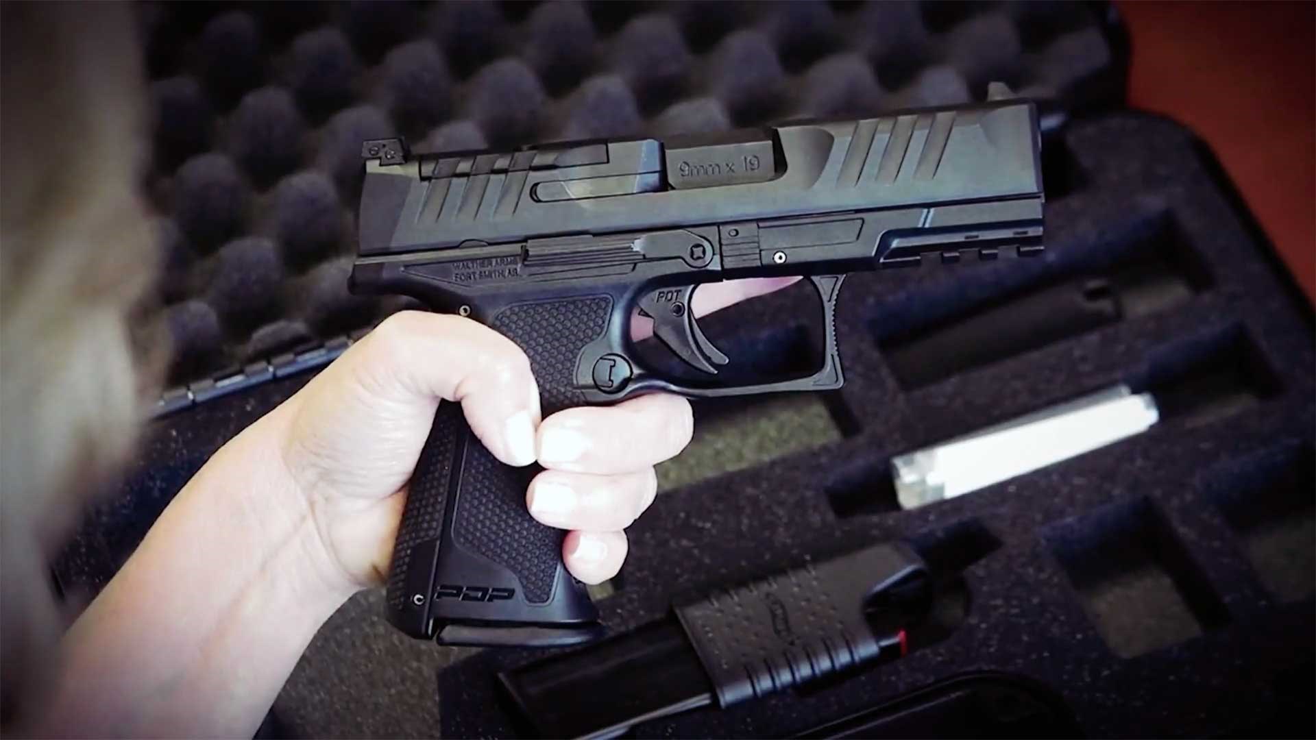A woman holds the Walther PDP F-Series handgun over an open, foam-lined, black gun case.
