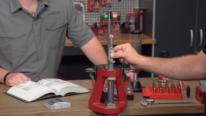 Two men at a reloading bench with tools adjusting a Hornady Iron Press.