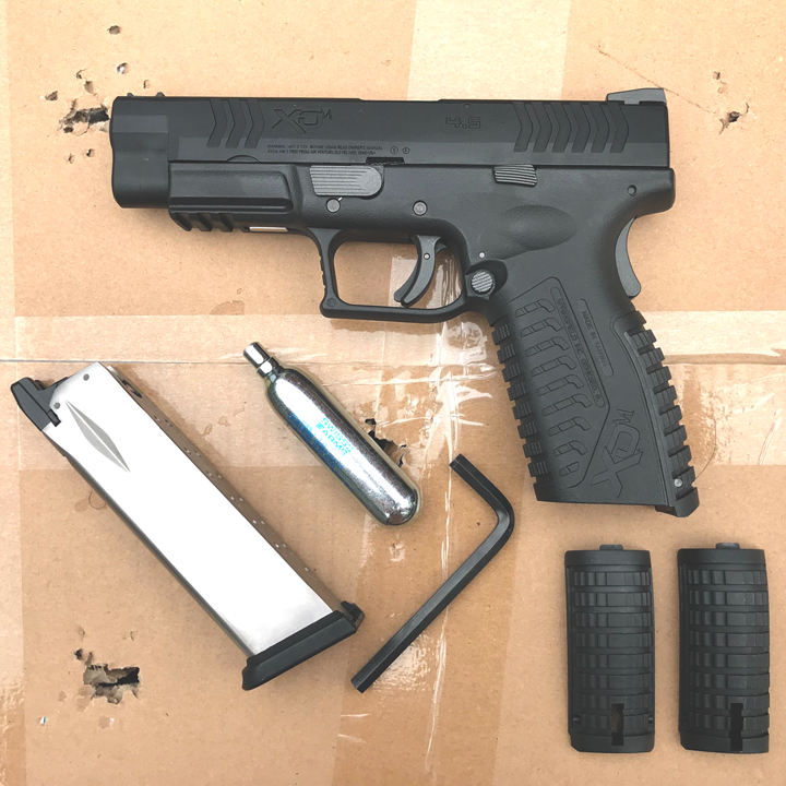 Left-side view of Springfield XDM air-powered pistol with accessories shown on a cardboard box.