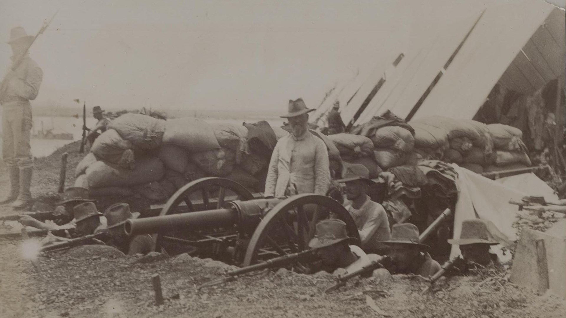 Company F in bunker with sandbags tent behind hotchkiss machine gun on wheels soldier guarding with rifles