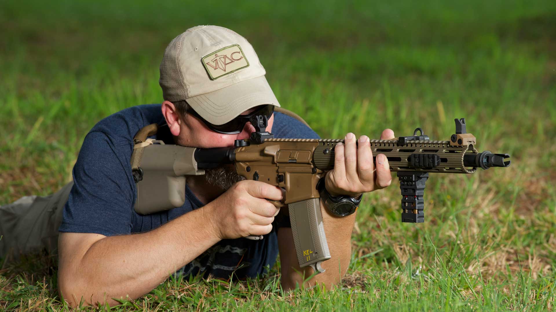 man grass rifle shooting outdoors blue shirt green gun