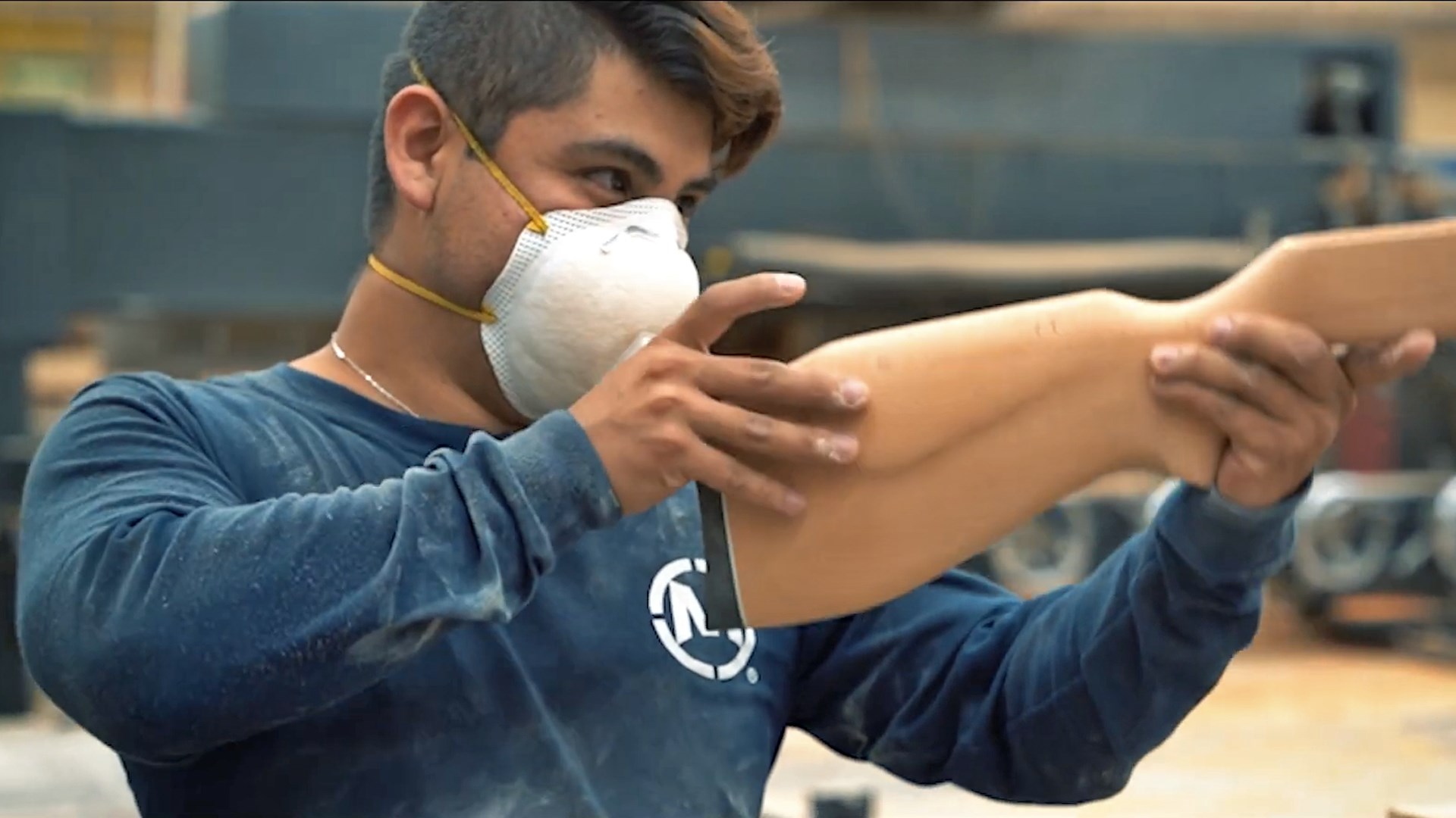 Man wearing a white mask examining the finish on a wooden rifle stock.