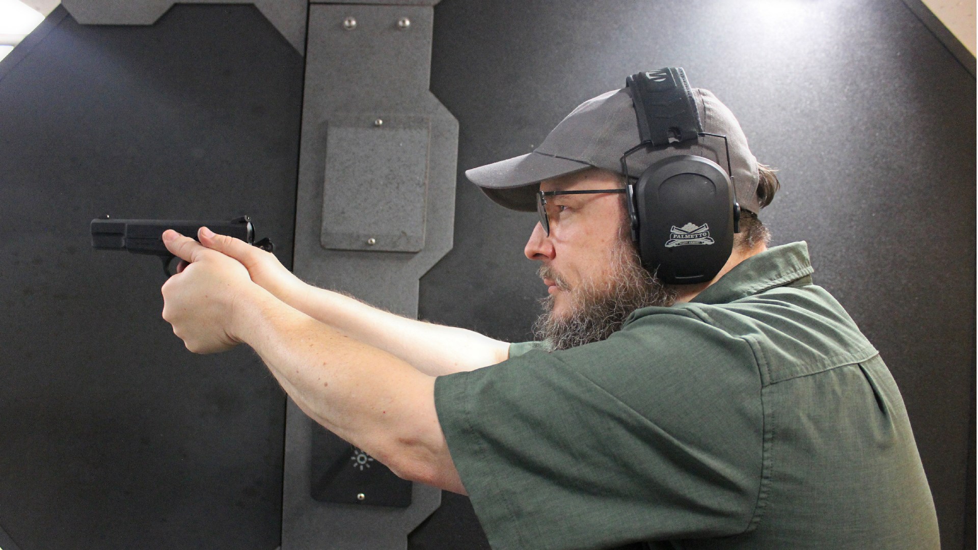 Author B. Gil Horman shown shooting Centurion 14 High-Power clone pistol indoor range wearing protective shooting gear ballcap and green shirt